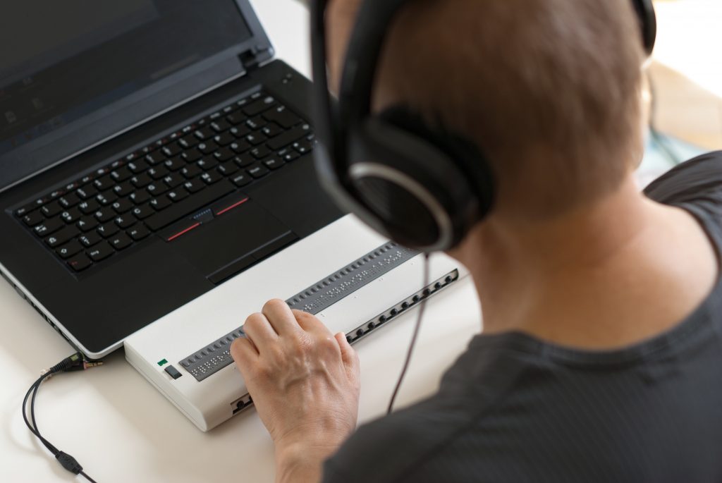 Malvoyant travaillant sur ordinateur avec une technologie d'assistance ; afficheur braille et lecteur d'écran.